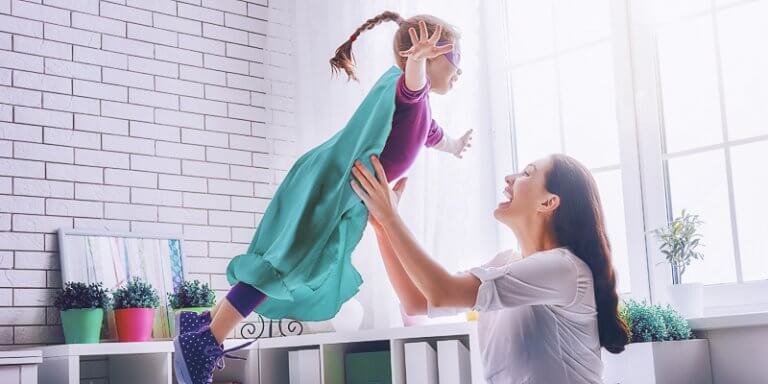 Mãe levantando sua filha, brincando de faz de conta de super-herói na cama