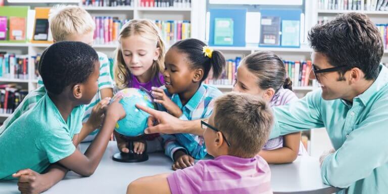 crianças e professor em sala de aula ao redor de um globo terrestre