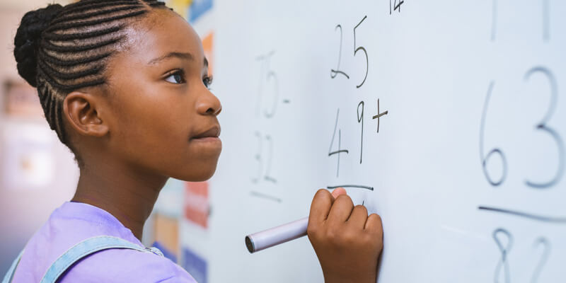 racismo na escola: criança negra resolvendo um exercício na lousa da sala de aula