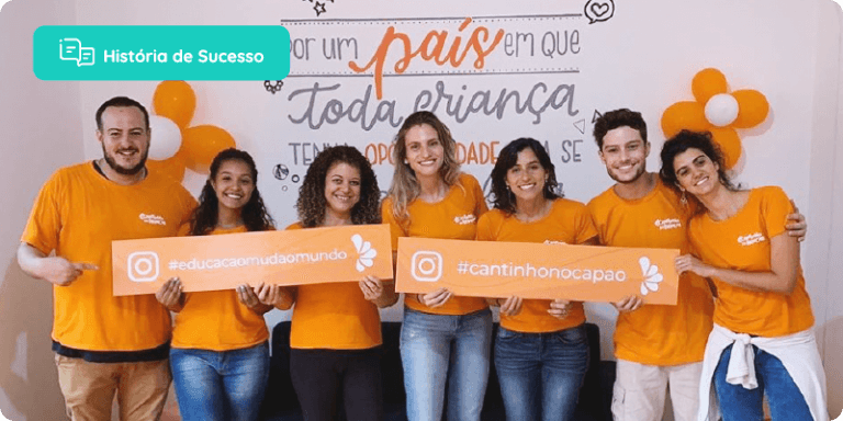 Equipe da escola, todos de camisa laranja, segurando uma placa com hashtag educação muda o mundo e a na outra placa o instagram da escola.