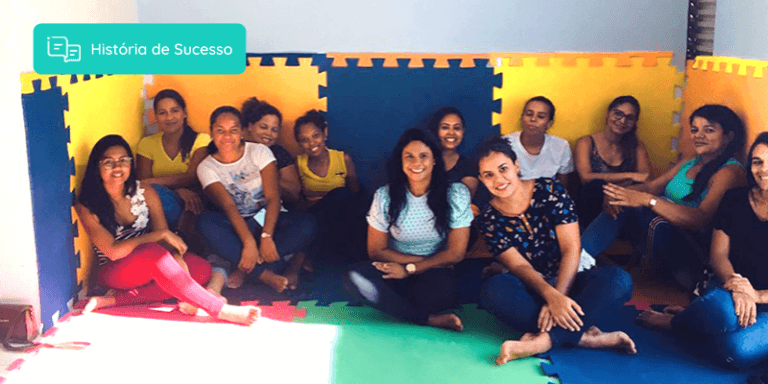 Colaboradores da escola Baby Camp sentados lado a lado em uma sala e sorrindo para a foto