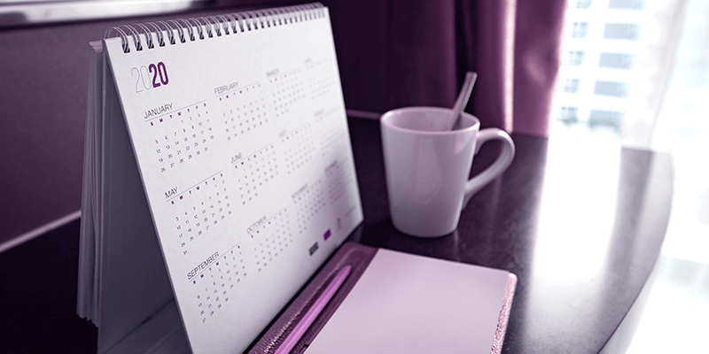 Calendário de 2020 sobre mesa ao lado de xícara de café, representando o ano letivo escolar