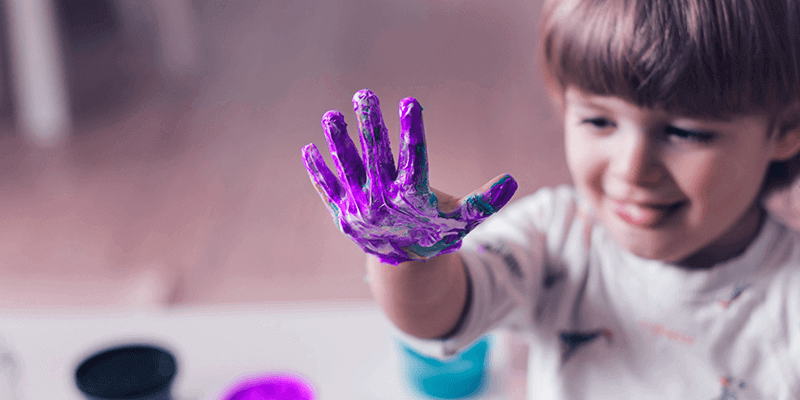 Criança com mão de cheia de tinta brincando com arte da Educação Infantil