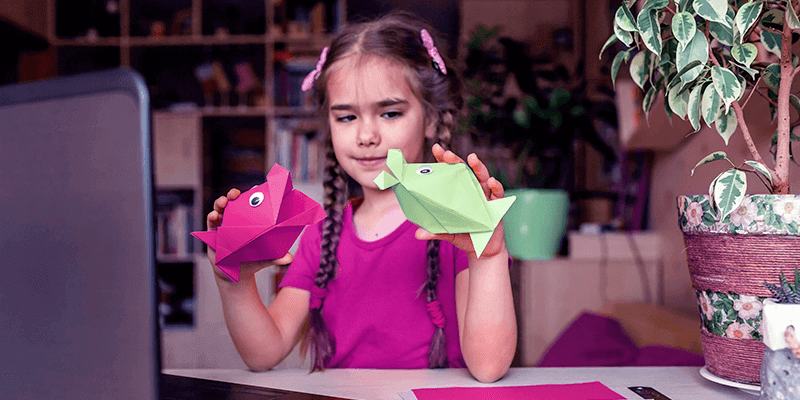 Menina fazendo atividades de Educação Infantil brincando com peixes de papel em frente ao notebook