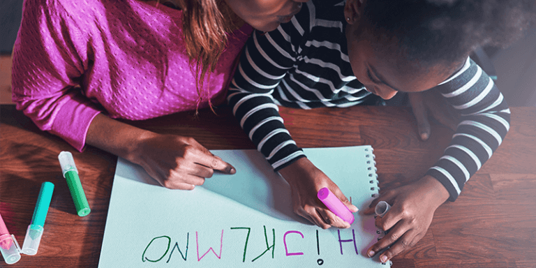 Alfabetização em casa com criança e mãe escrevendo letras em papel
