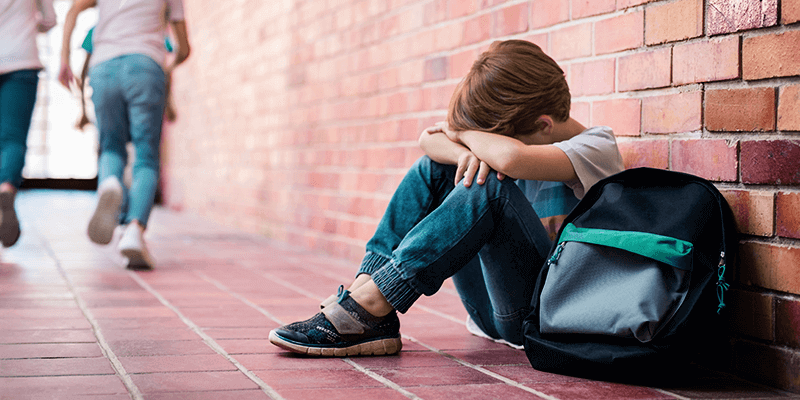 Bullying na escola: criança sentada no corredor com a cabeça apoiada nas pernas