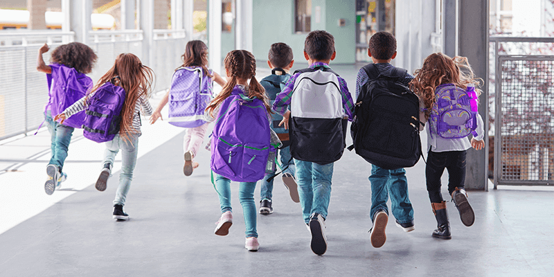 Alunos com mochilas correndo no corredor da escola no primeiro dia de aula
