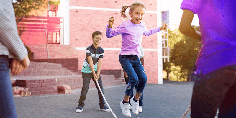 Crianças brincando com de pular corda no pátio da escola