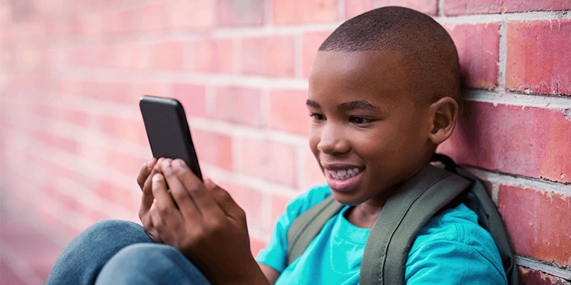 Tempo de tela: criança de mochila sorrindo e utilizando celular