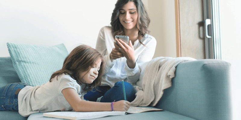 Mãe e filha na sala de casa fazendo tarefa e lendo comunicado escolar pelo celular