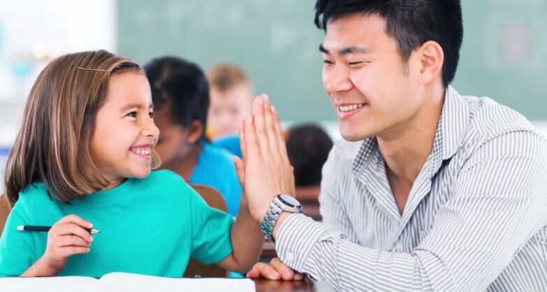 Aluna e professor batem as mãos sorrindo na sala de aula